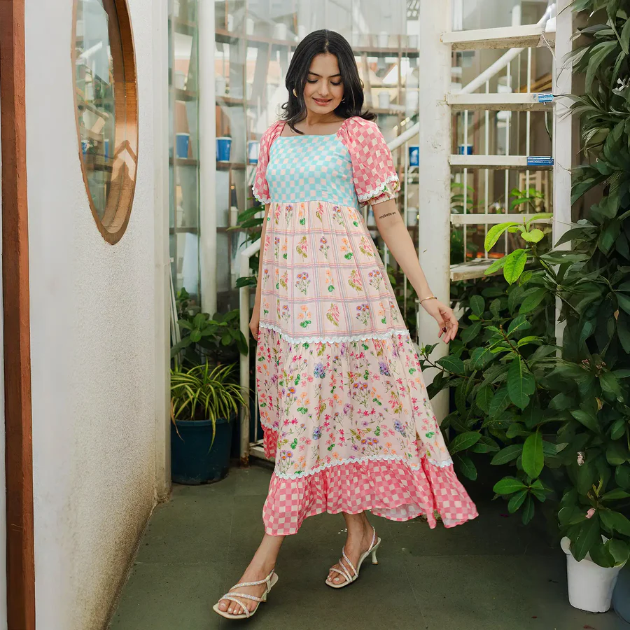 Woman in colorful printed patchwork dress near indoor plants.