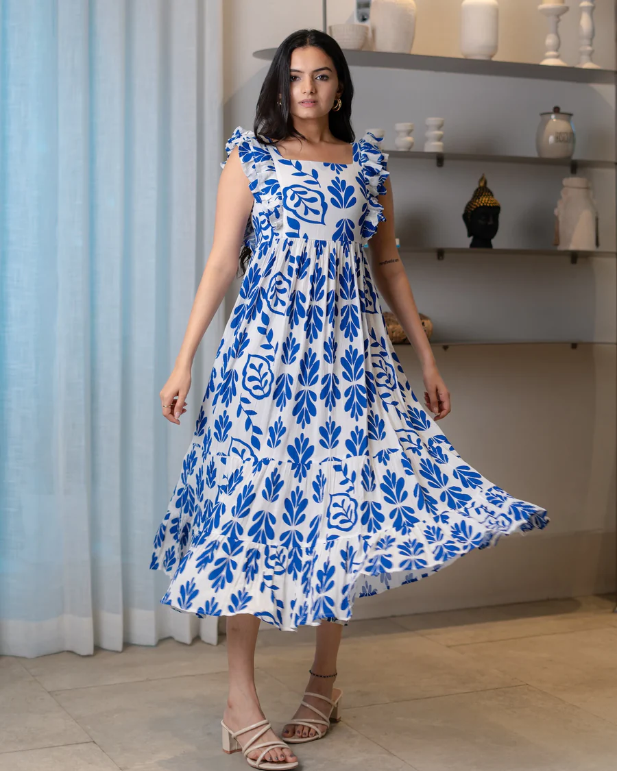 Woman in white and blue floral ruffle dress posing indoors.